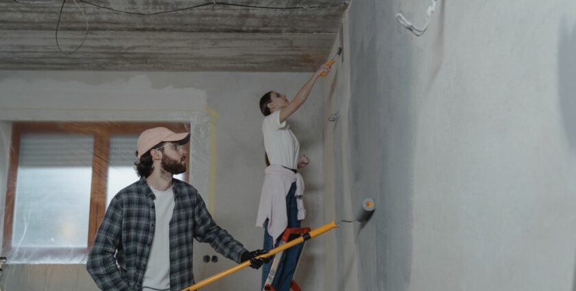 Couple peignant les murs et plafond d'une pièce en rénovation avec rouleau et pinceau