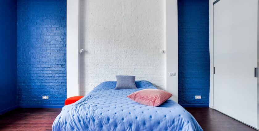 Chambre adulte avec mur peint en bleu vif, literie bleue assortie et parquet bois foncé