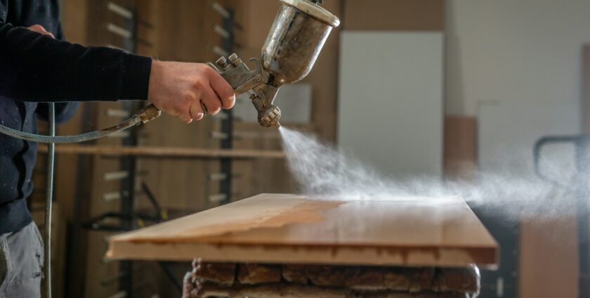 Application de laque sur un meuble en bois avec pistolet HVLP en atelier